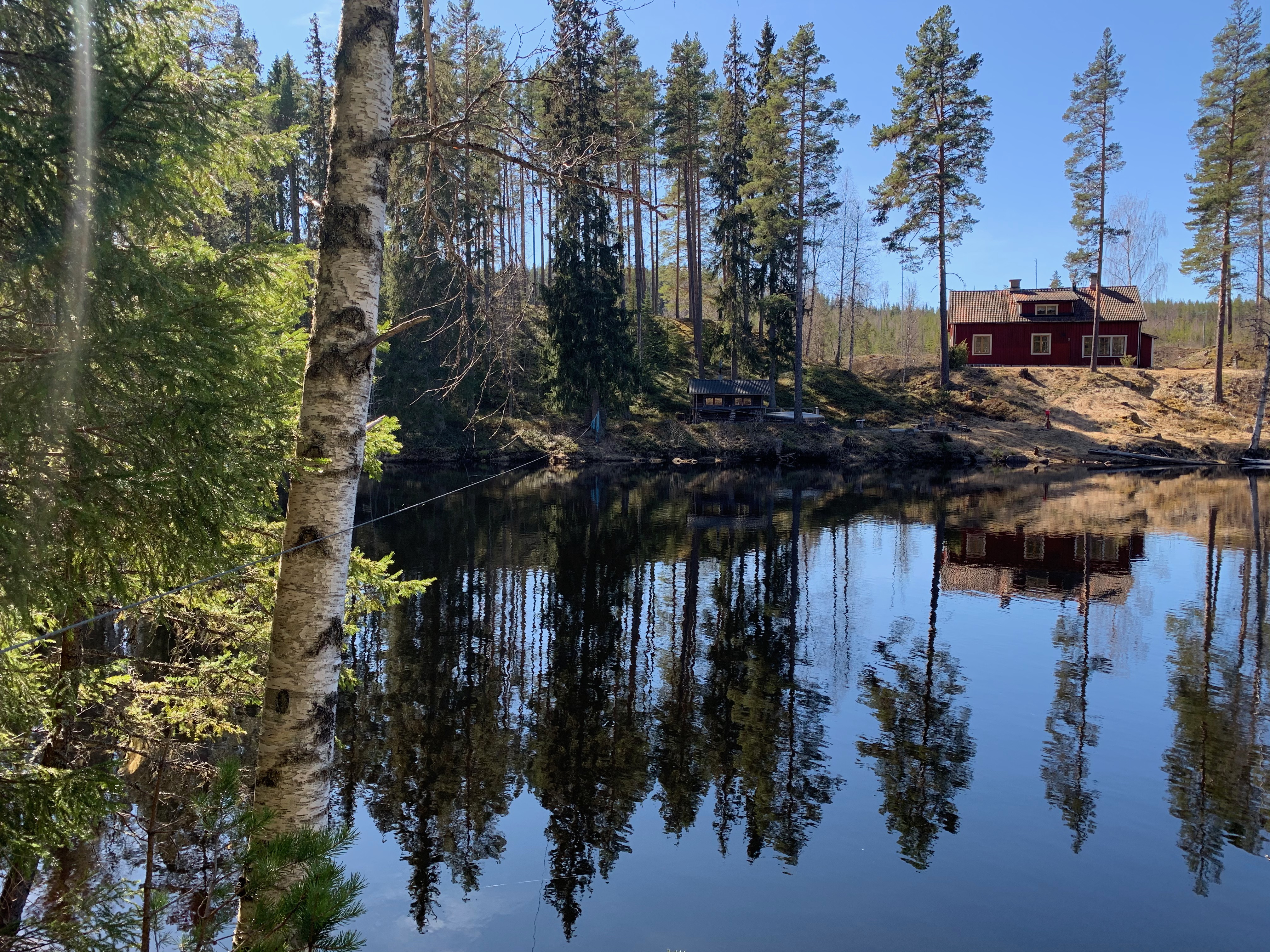 Vildmark, sjö och ett rött hus bortanför sjön.