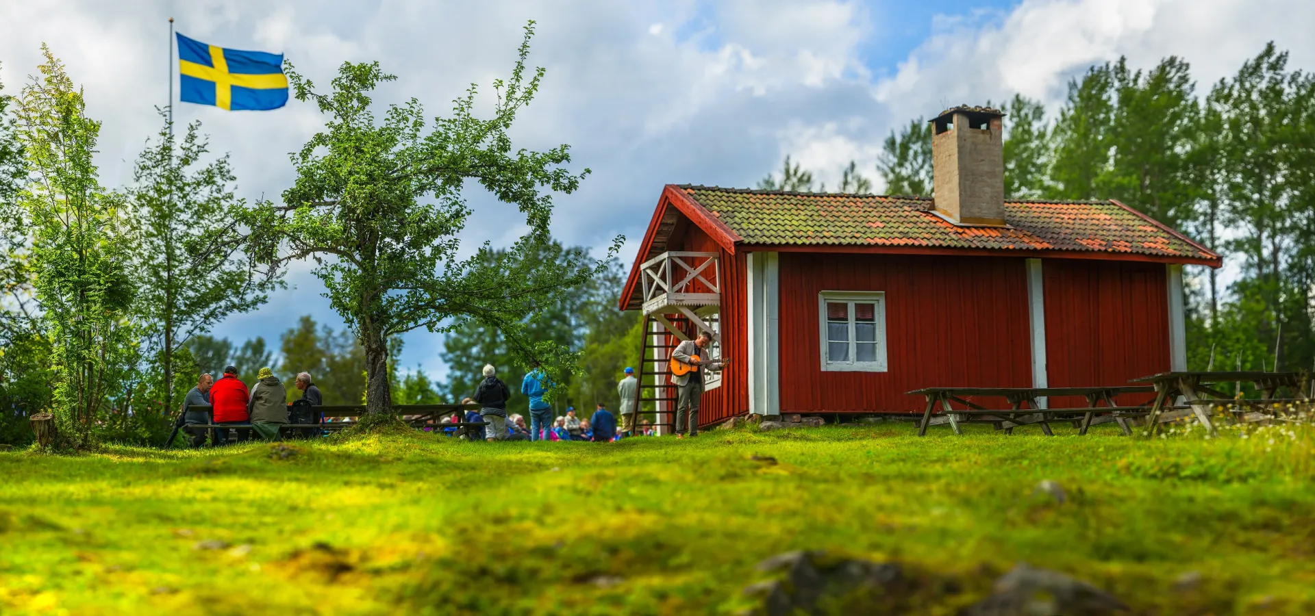 Rödmålad stuga med en flaggstång på gården.