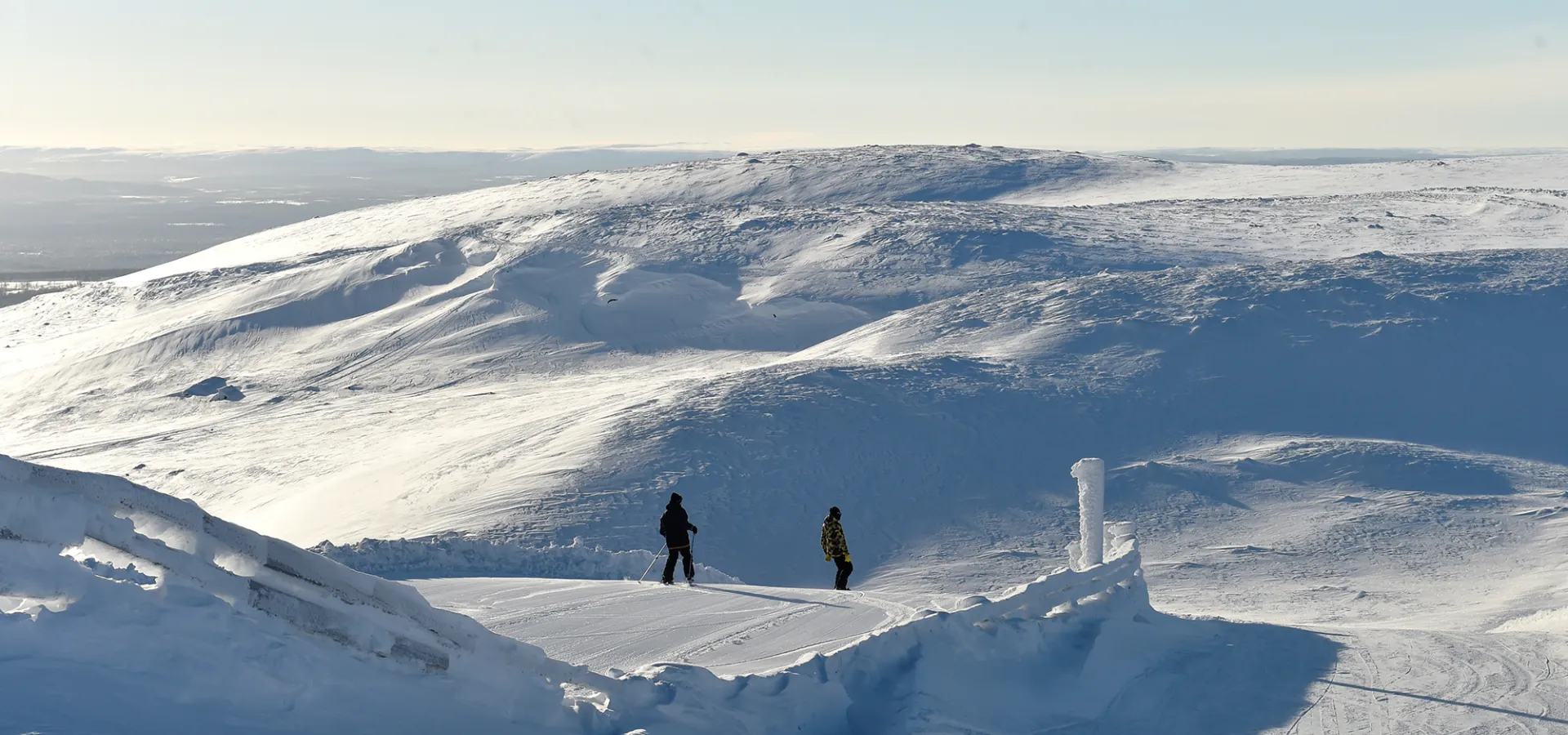 Två personer åker skidor nedför en solig backe i fjällen.