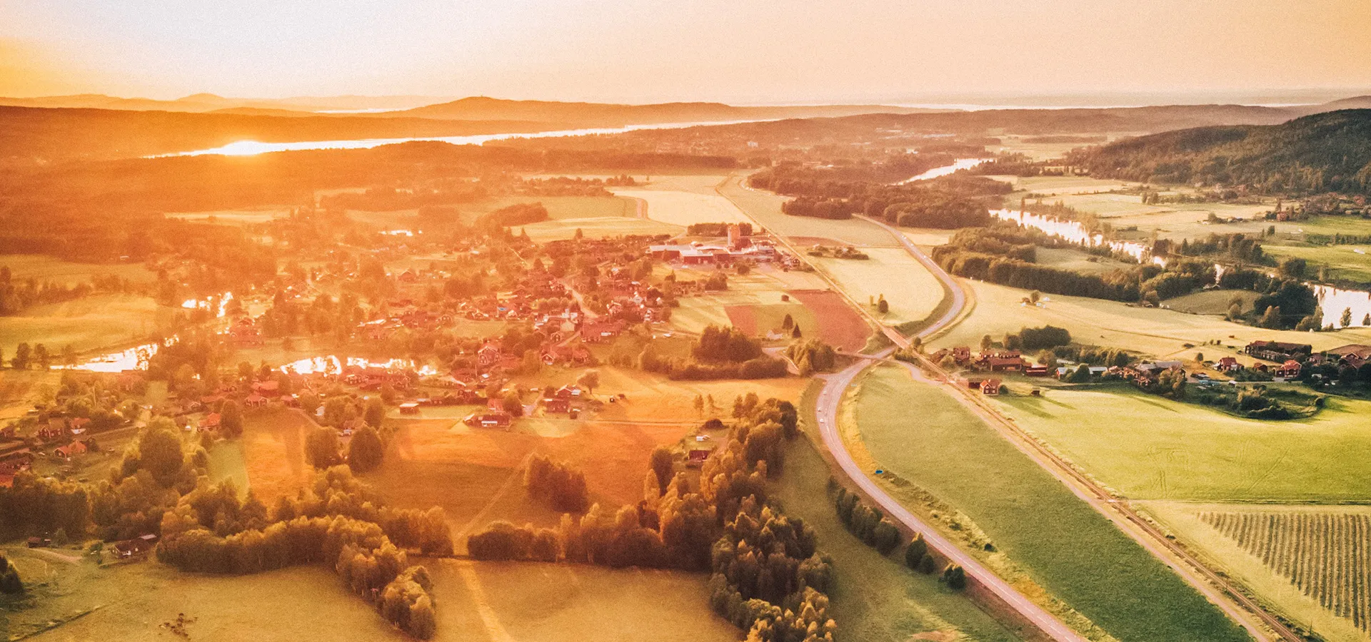 Solnedgång över ett vackert grönt landskap med röda hus och små dammar.