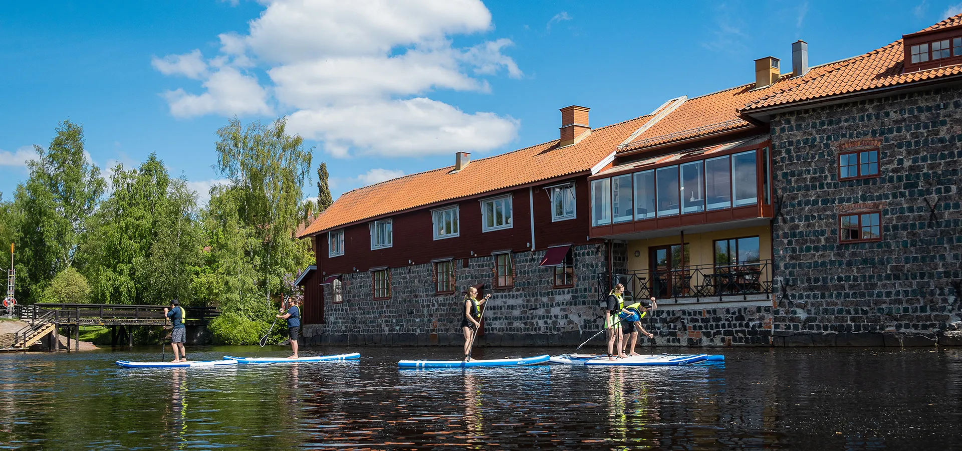 En grupp paddlar SUP i vattnet framför ett rött hus.