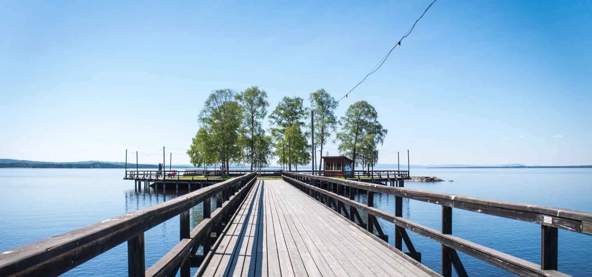 Långbryggan i Rättvik, blått vatten och himmel, en ö med träd längst ut.