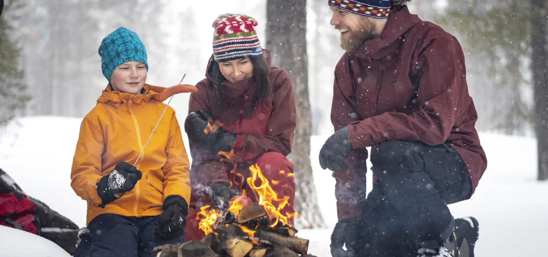 Familj värmer sig runt en öppen eld i snörikt landskap.