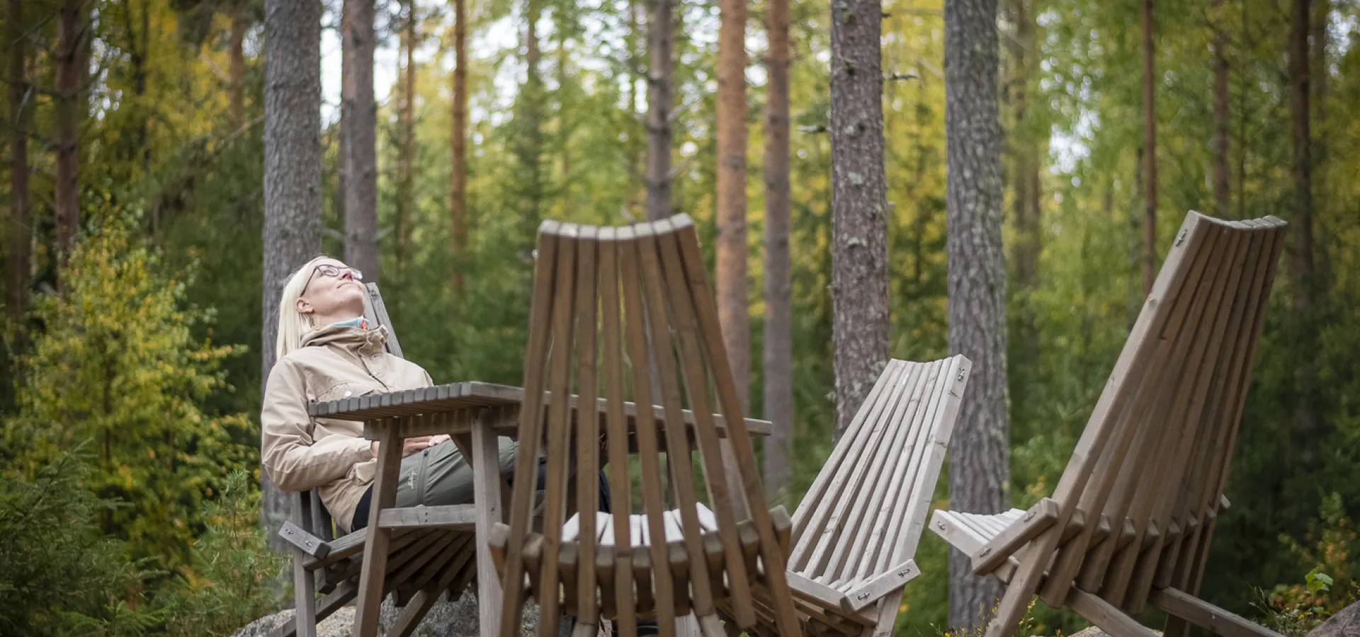 Kvinna sitter i skogen och tittar upp mot himlen.