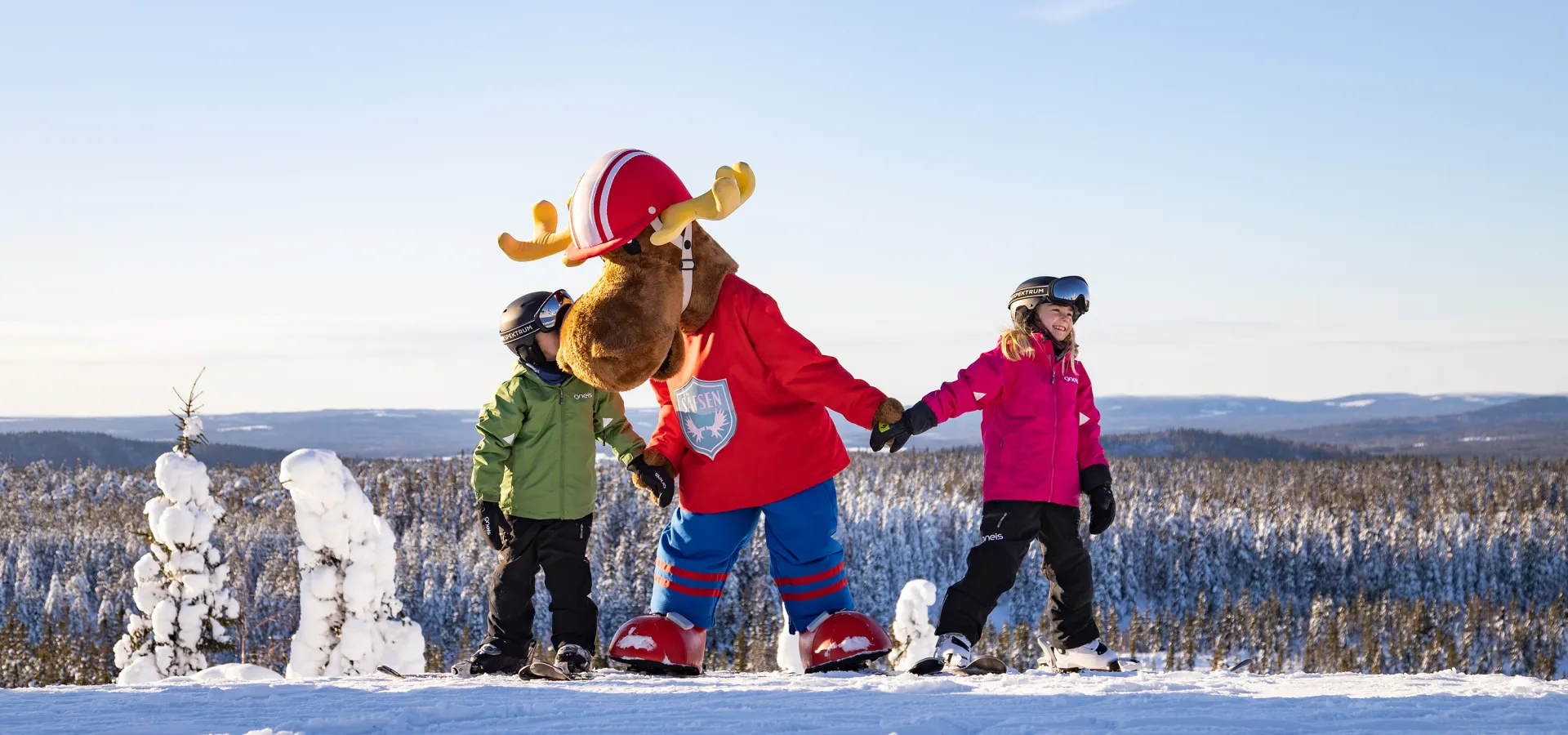 Två barn på skidor håller en person utklädd till älg i händerna.