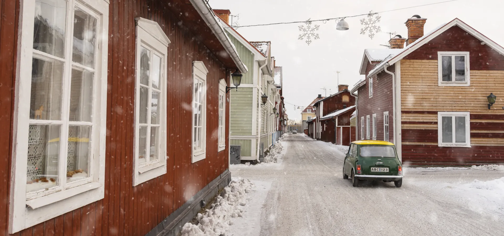 Bil åker mellan faluröda hus vintertid.