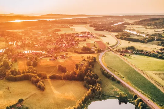 Solnedgång över ett vackert grönt landskap med röda hus och små dammar.