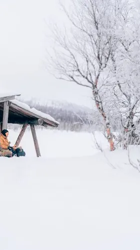 Par som sitter vid en slogbod i vintermiljö.