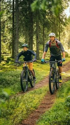 Man och barn som cyklar i skogen. 