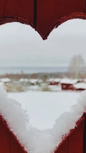 Titthål över vinterlandskap genom rött plank.