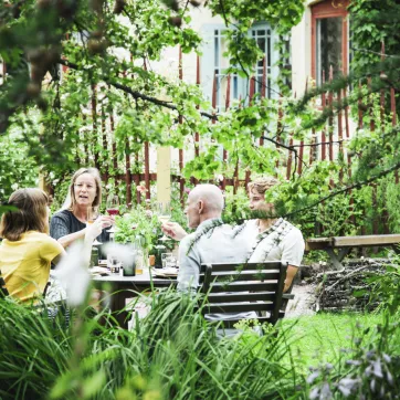 Fyra personer sitter kring ett bort utomhus bland lummig grönska.