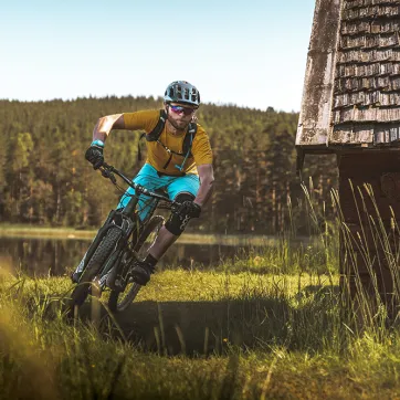 En man cyklar mountainbike bredvid en liten stuga.