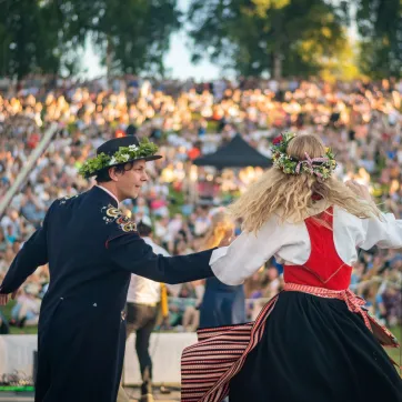 Par i folkdräkt som uppträder under midsommarfirande.