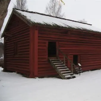 Röd äldre timmerlada, två dörrar av mindre  modell med en enkel trapp upp till dörren, vinterbild.