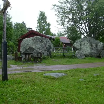 Stora stenar och en fäbodstuga bakom.