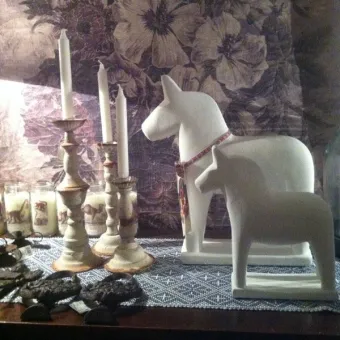 Two white dalahorses in ceramics, three candlesticks, floral pattern in the background.