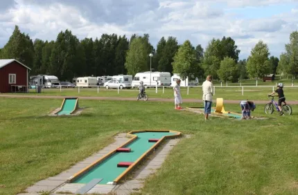 Personer som spelar på golfbanan med husvagnar i bakgrunden. 