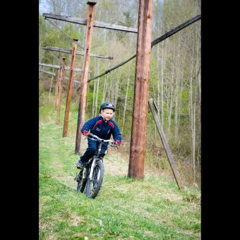 A boy cycling along a grass path, next to the path are poles on display.