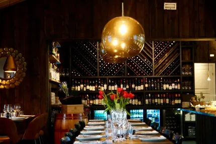Ett uppdukat långbord med en vas med röda tulpaner i restaurangen. I bakgrunden en vägghylla fylld med viner.