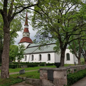 Norrbärke kyrka och kyrkogården med grönskande träd.