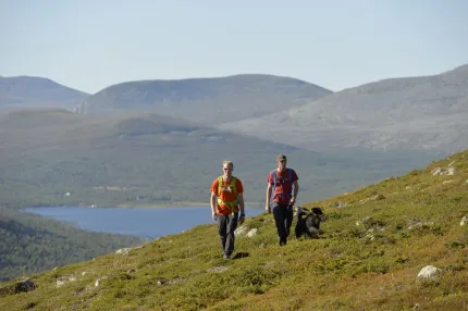 Two hikers with dogs, Grövelsjön and mountains in the background.