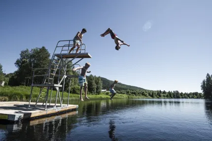 Fyra pojkar hoppar ut i vattnet från trampolin.