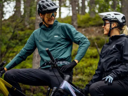 En man och en kvinna i cykelkläder på varsin cykel, som står stilla, skog i bakgrunden.
