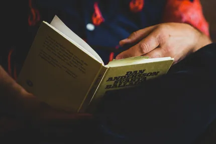 En person sitter med med en bok i knät och läser.