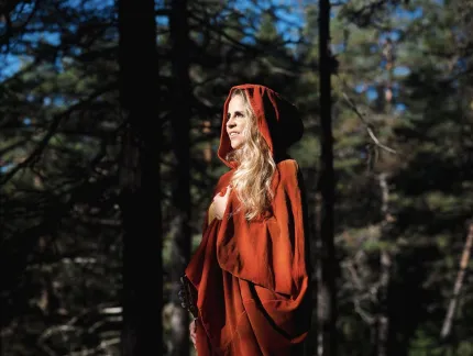 Lisa Miskovsky iklädd röd mantel med huva i skogen med sol i ansiktet.