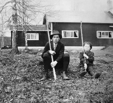 Dan Andersson och liten pojke sittandes i trädgården med varsin lång pinne i handen på Brunnsviks Folkhögskola.