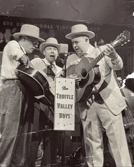 En svartvit bild, tre män i hatt, ljusa kläder och varsin gitarr.