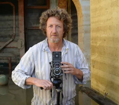 En man i randig skjorta, håller i en kamera.
