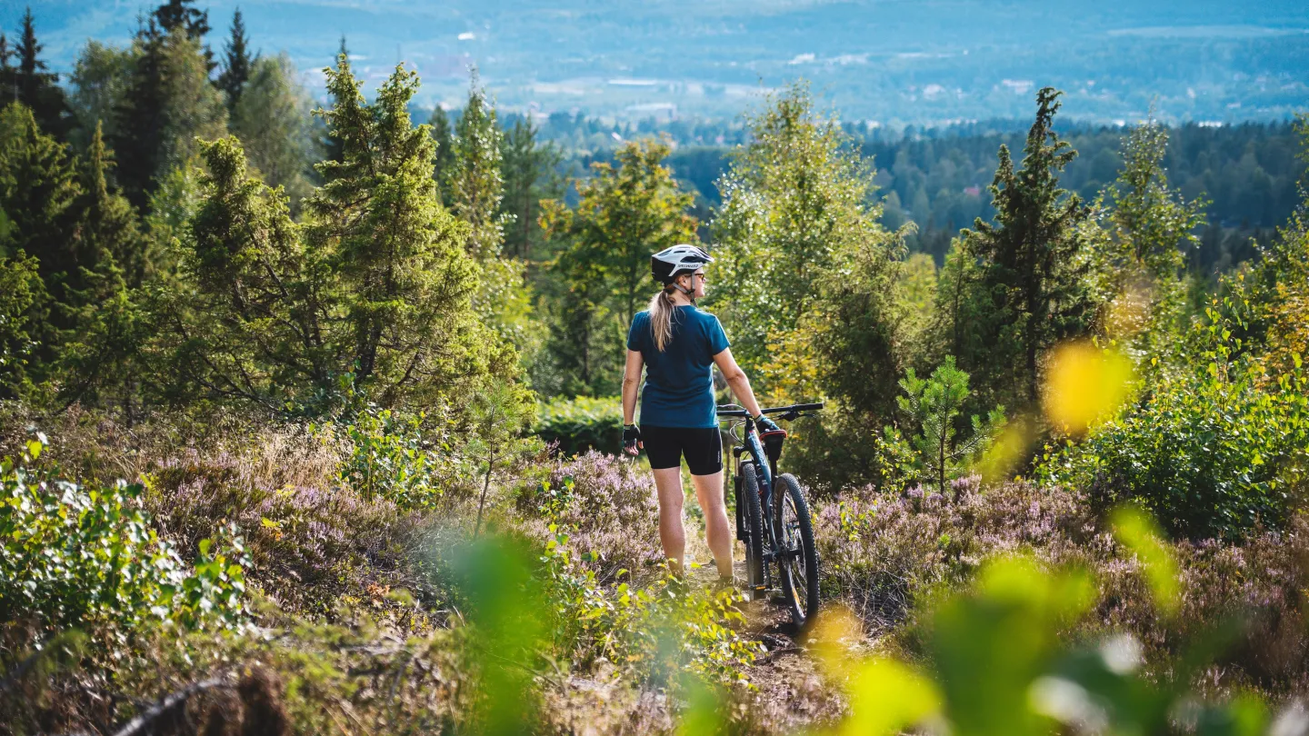 Tjej som står vid sin MTB i skogsmiljö.