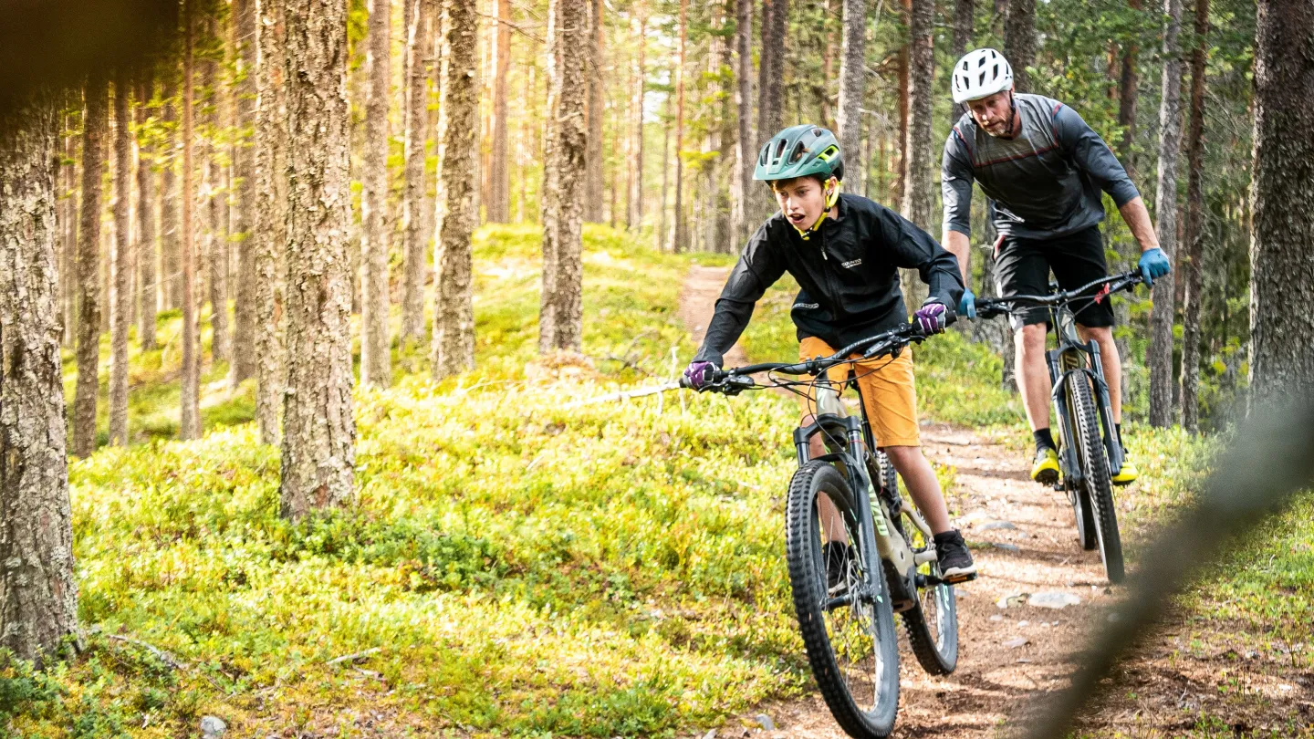 Far och son cyklar längs en skogsstig.