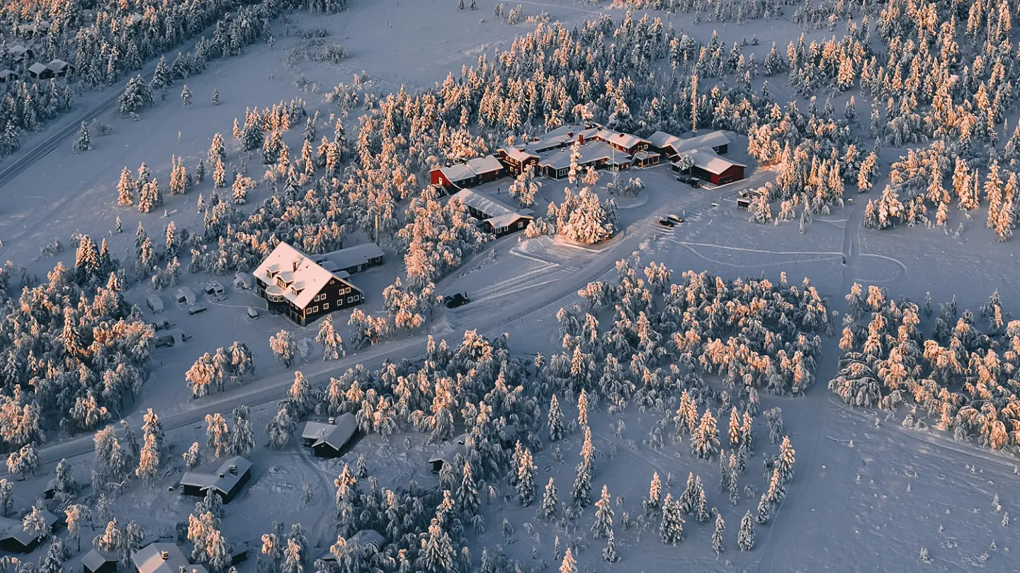 Flygfoto över stugor i fjälllandskap.