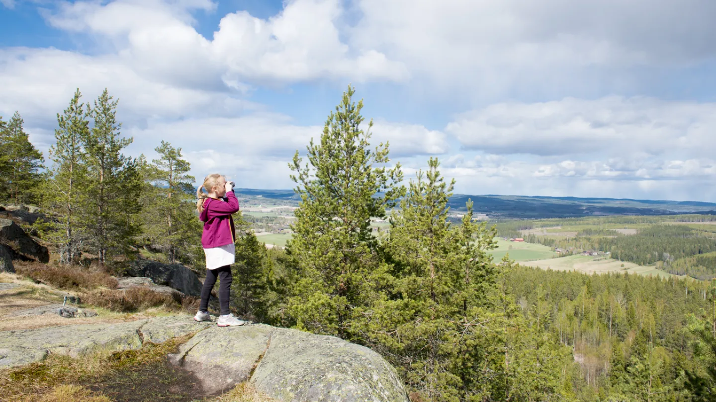 Tjej som står på en klippa med kikare.