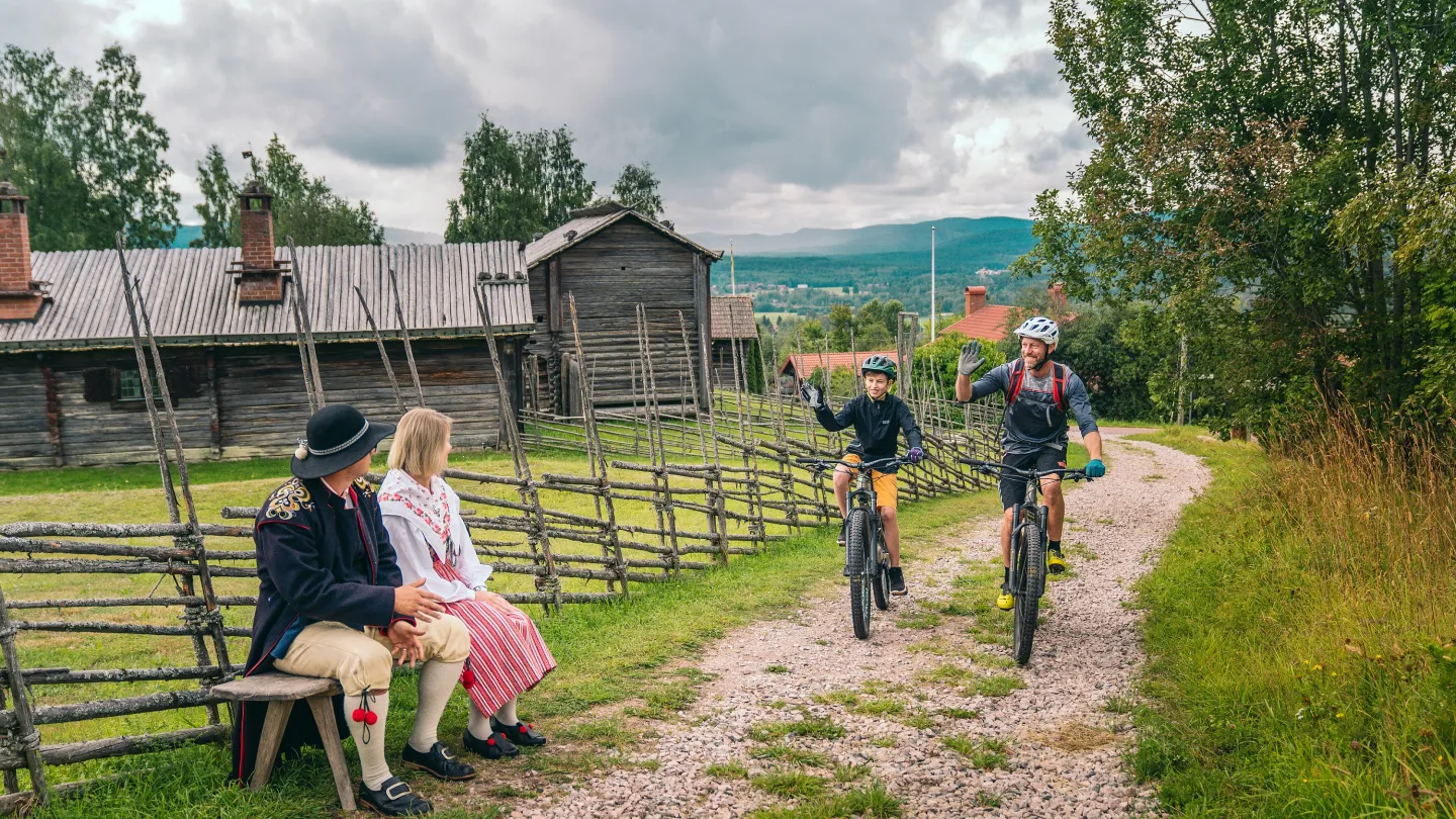 Två cyklister passerar två personer i folkdräkt.