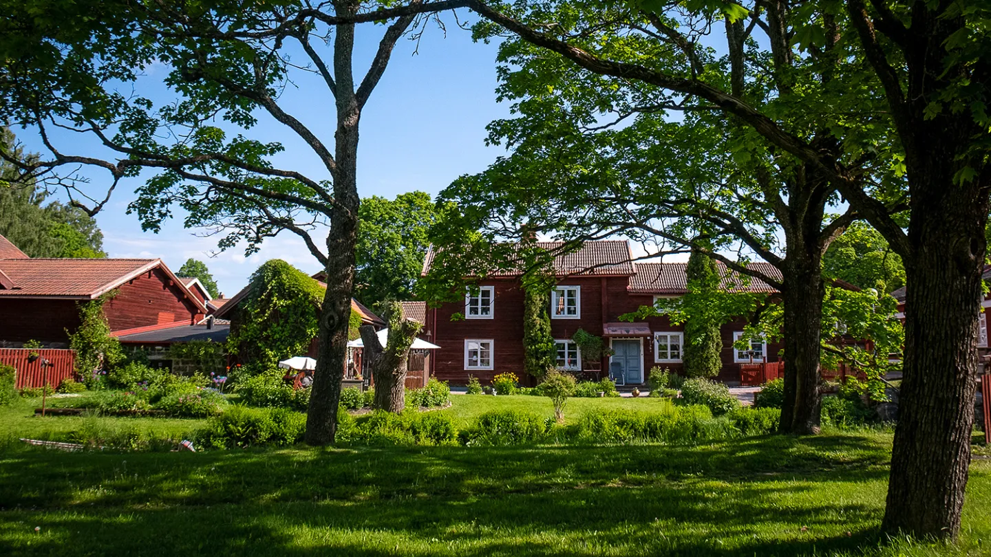 Gamla Byn i Avesta, röda äldre hus bland höga träd.