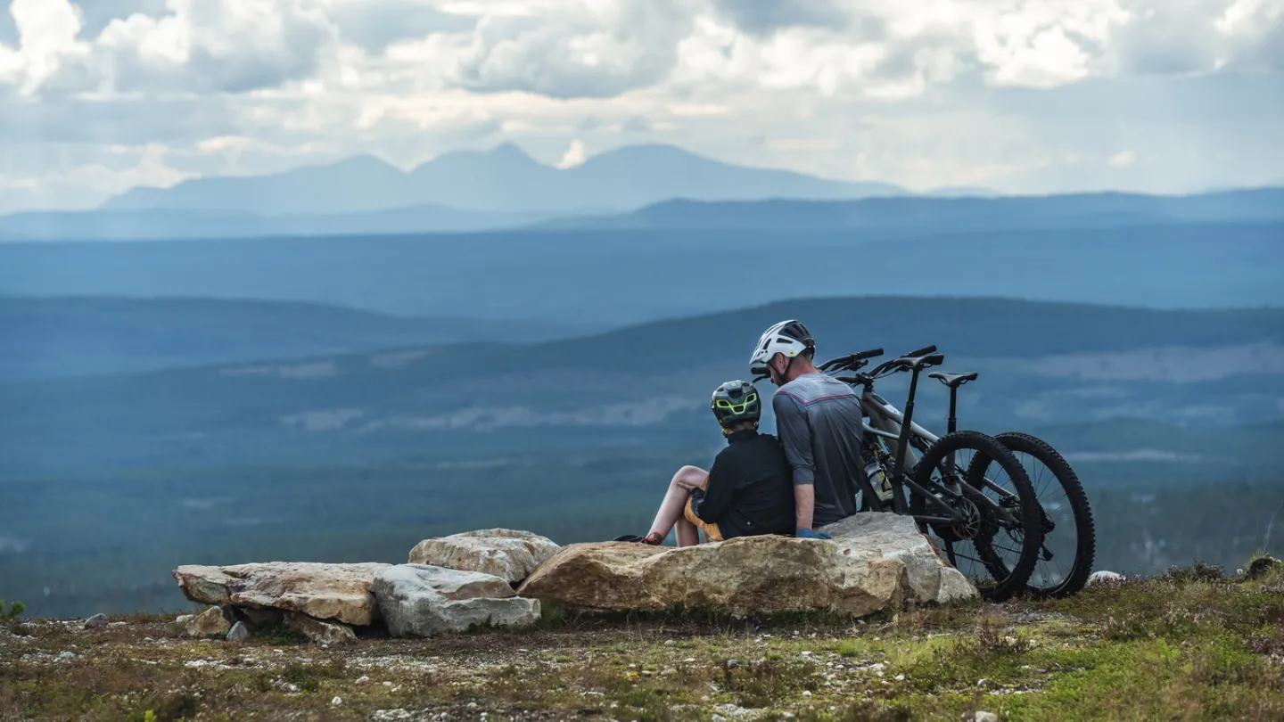 Två personer som sitter på ett fjäll vid sina cyklar.