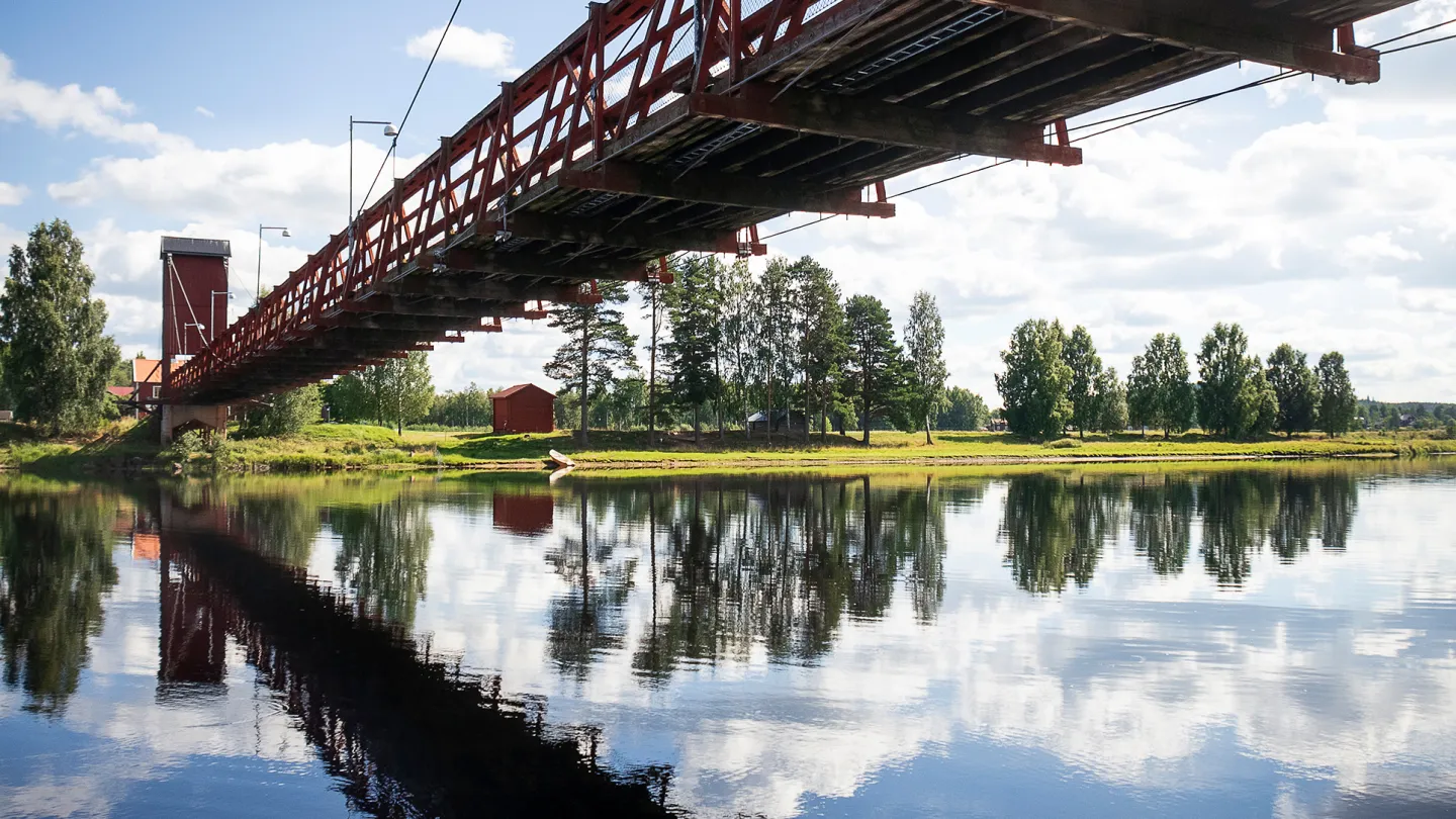 En lång bro speglar sig i vattnet under blå himmel.